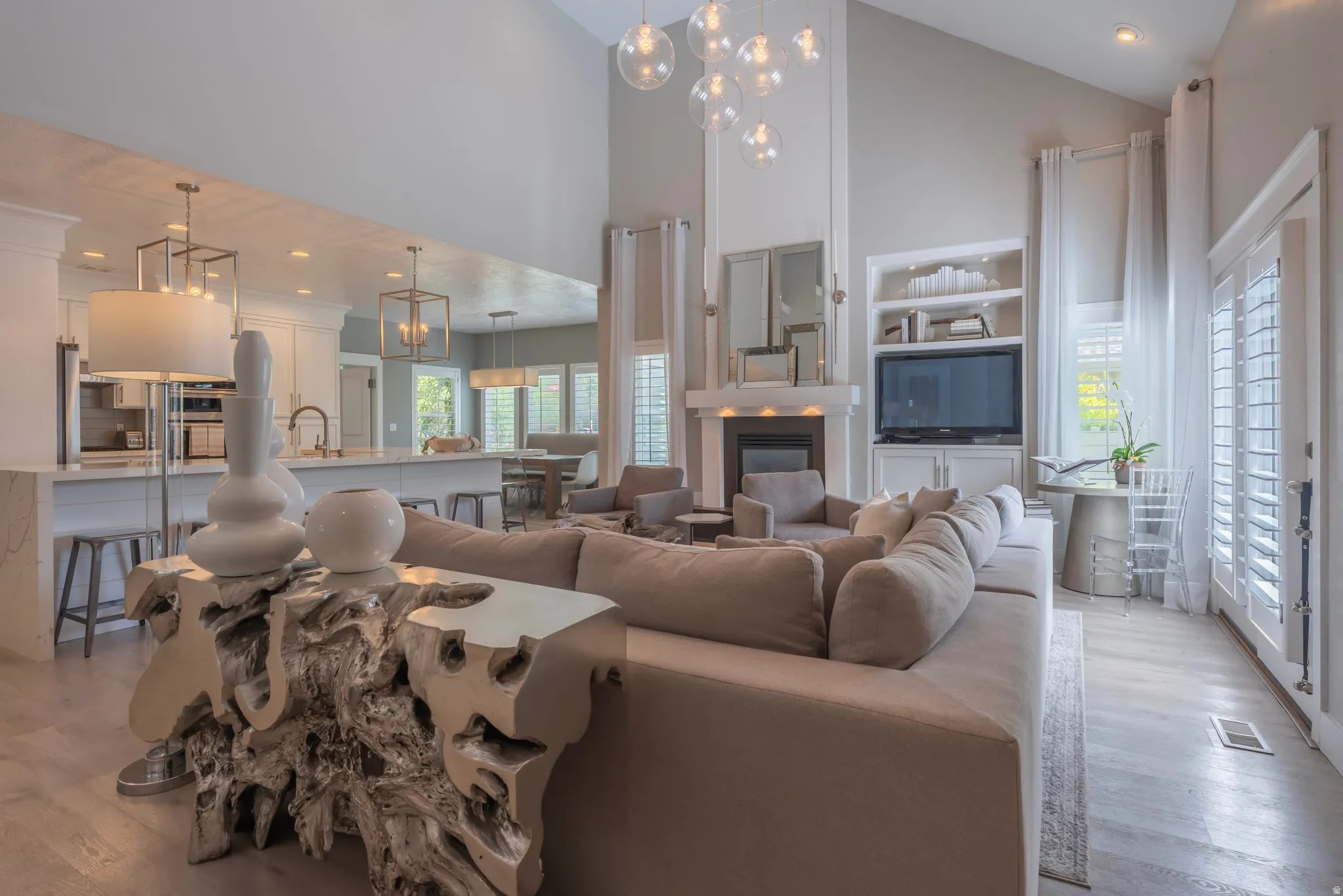 Vaulted ceilings, a built-in fireplace with a mantel, and shuttered doors define this bright living space
