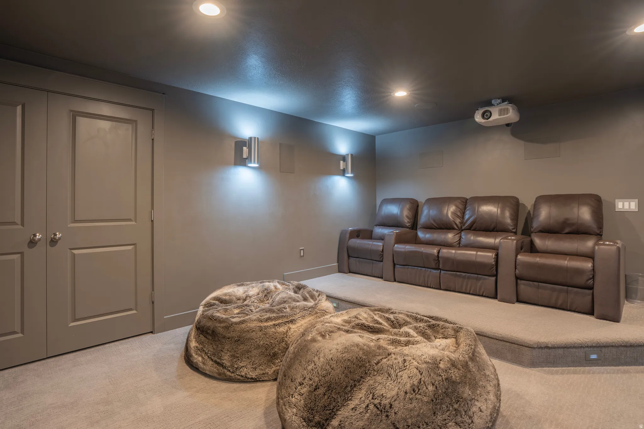 Dedicated media room featuring recessed lighting, wall-mounted sconces, and a ceiling-mounted projector