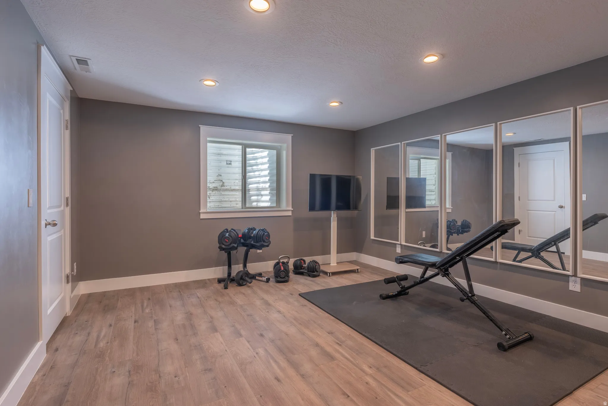 Recessed ceiling lighting, wood-finish flooring, white trim, and a window with a window well