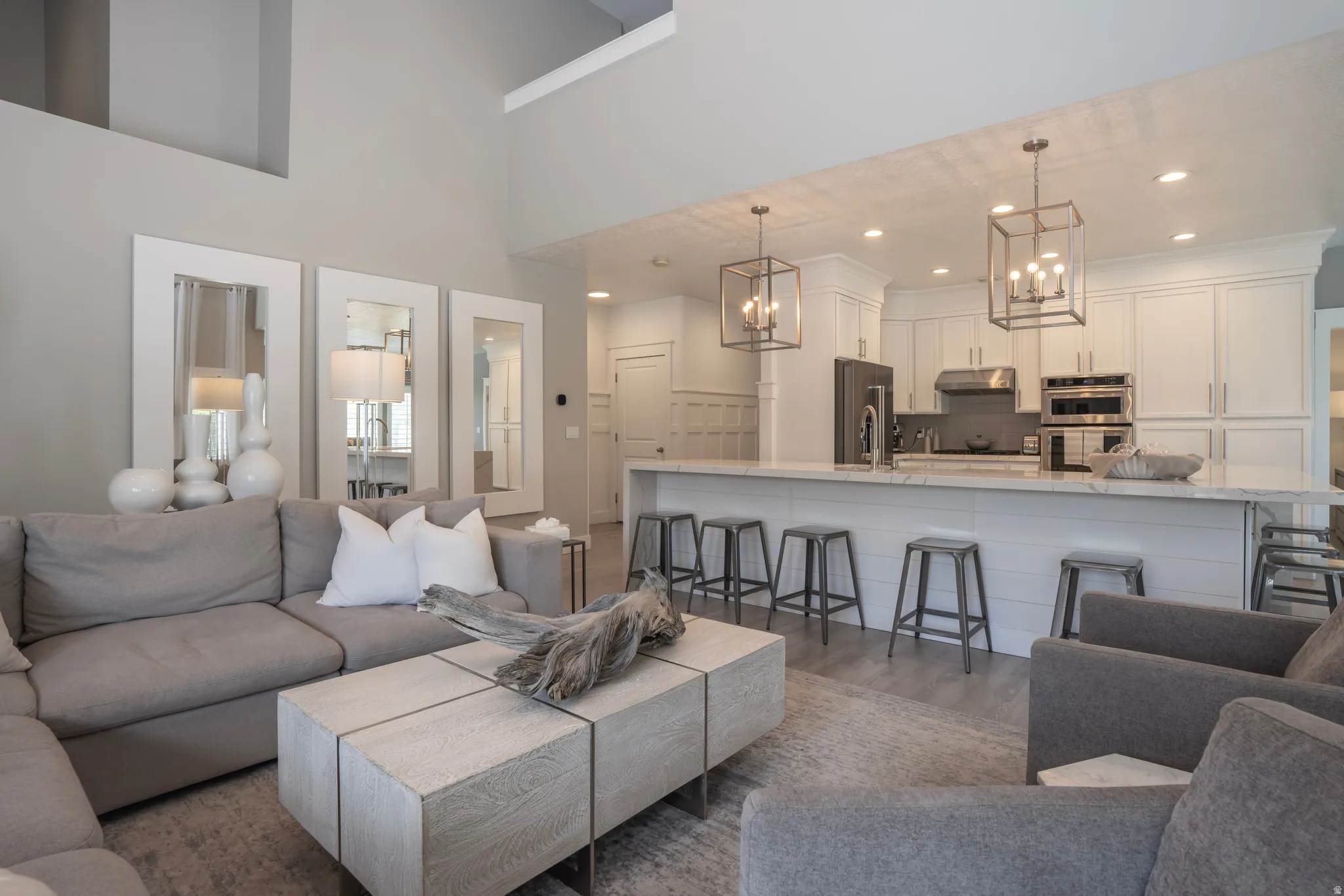 Open-concept living space featuring high ceilings, wood-finish flooring, and a kitchen with white cabinetry, stainless steel appliances, and a breakfast bar with pendant lighting