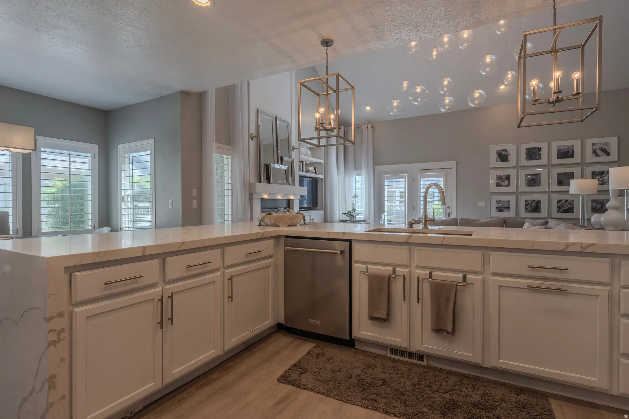 White cabinetry with brushed nickel hardware, light-toned countertops, built-in dishwasher, wood-finish flooring, and dual pendant lighting fixtures