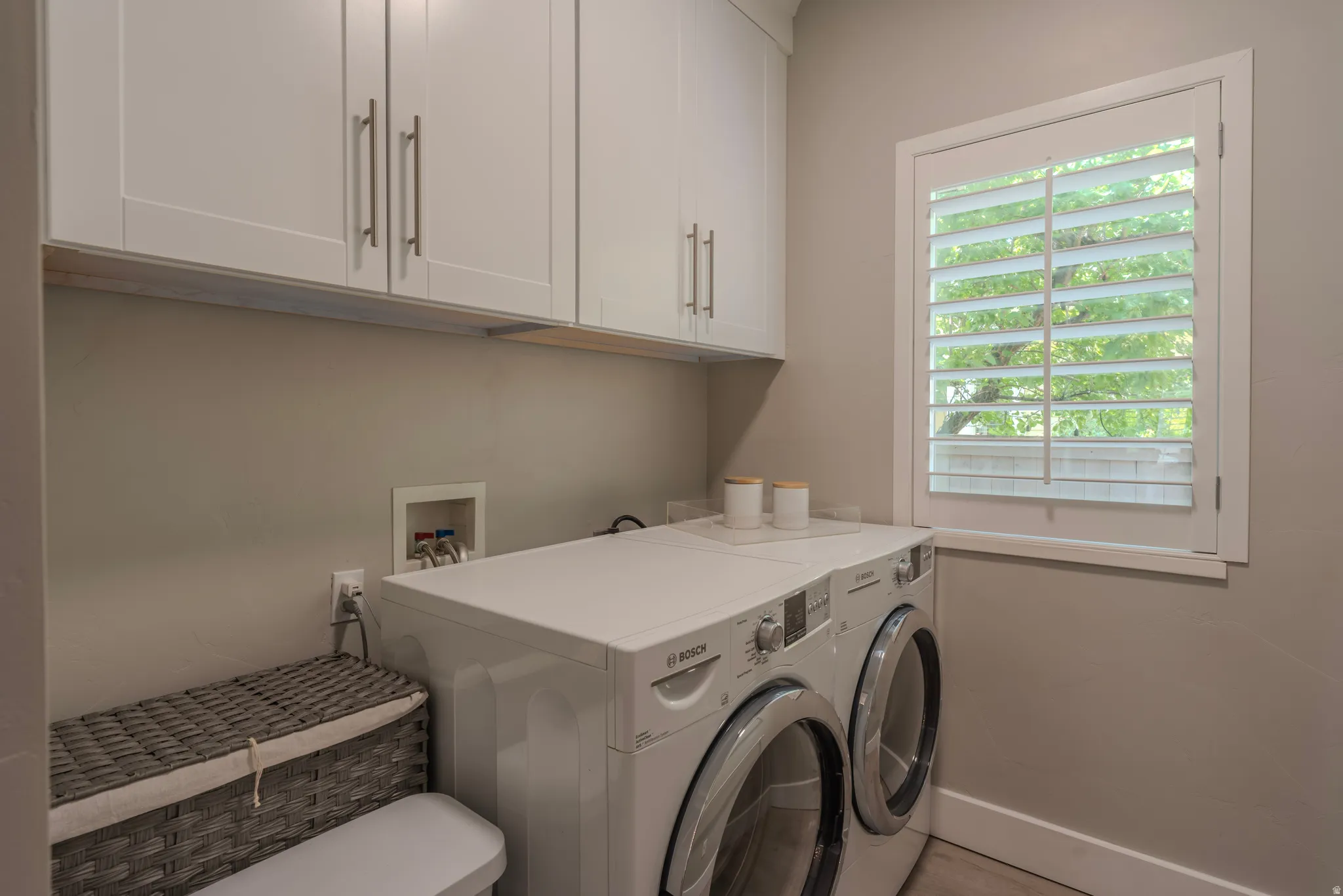 White shaker-style cabinetry with brushed nickel hardware and a window with plantation shutters