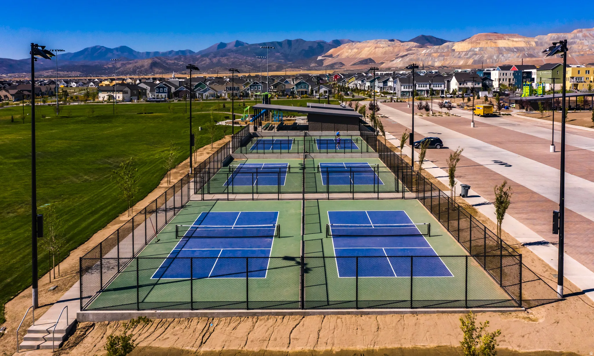 Multiple pickleball courts with perimeter fencing, adjacent open green space, and visible residential structures