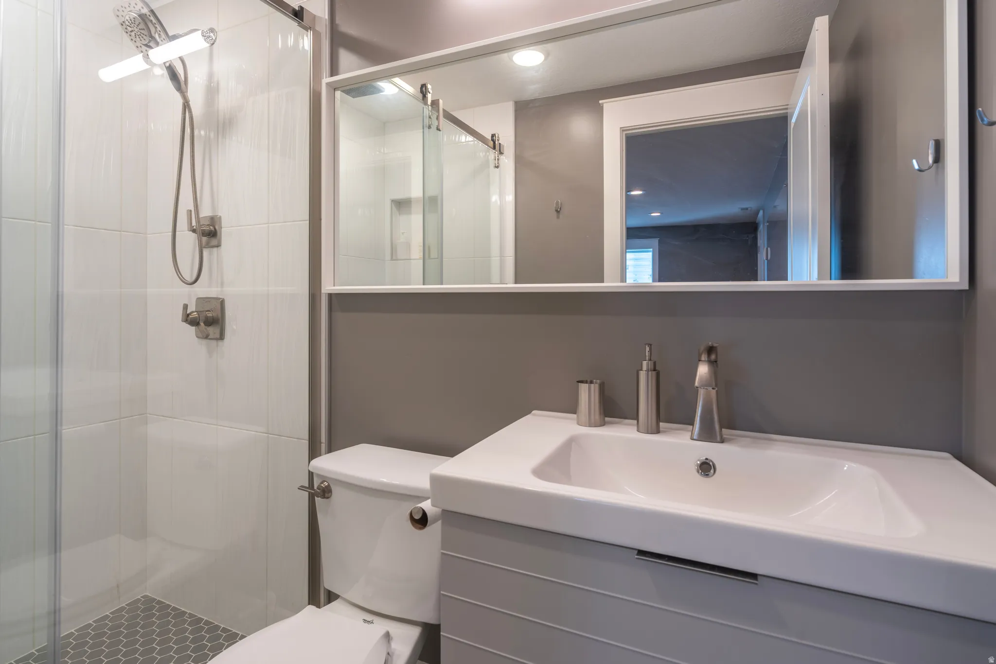 Glass-enclosed shower with white tiled walls and hexagonal floor tiles