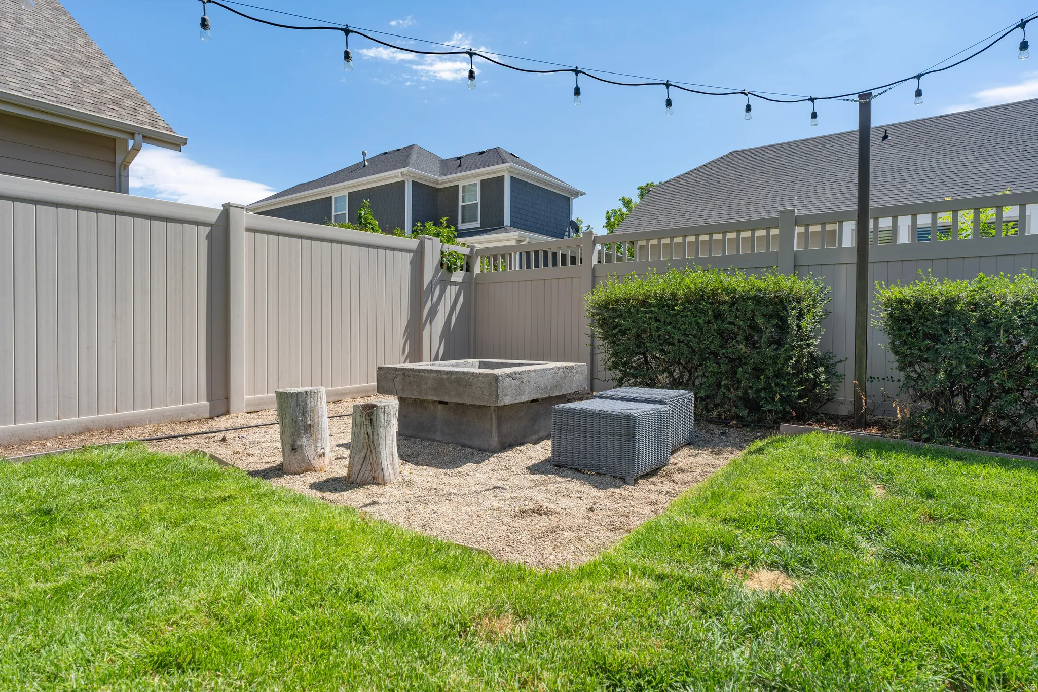 Manicured lawn with a concrete fire pit, string lighting, and privacy fencing