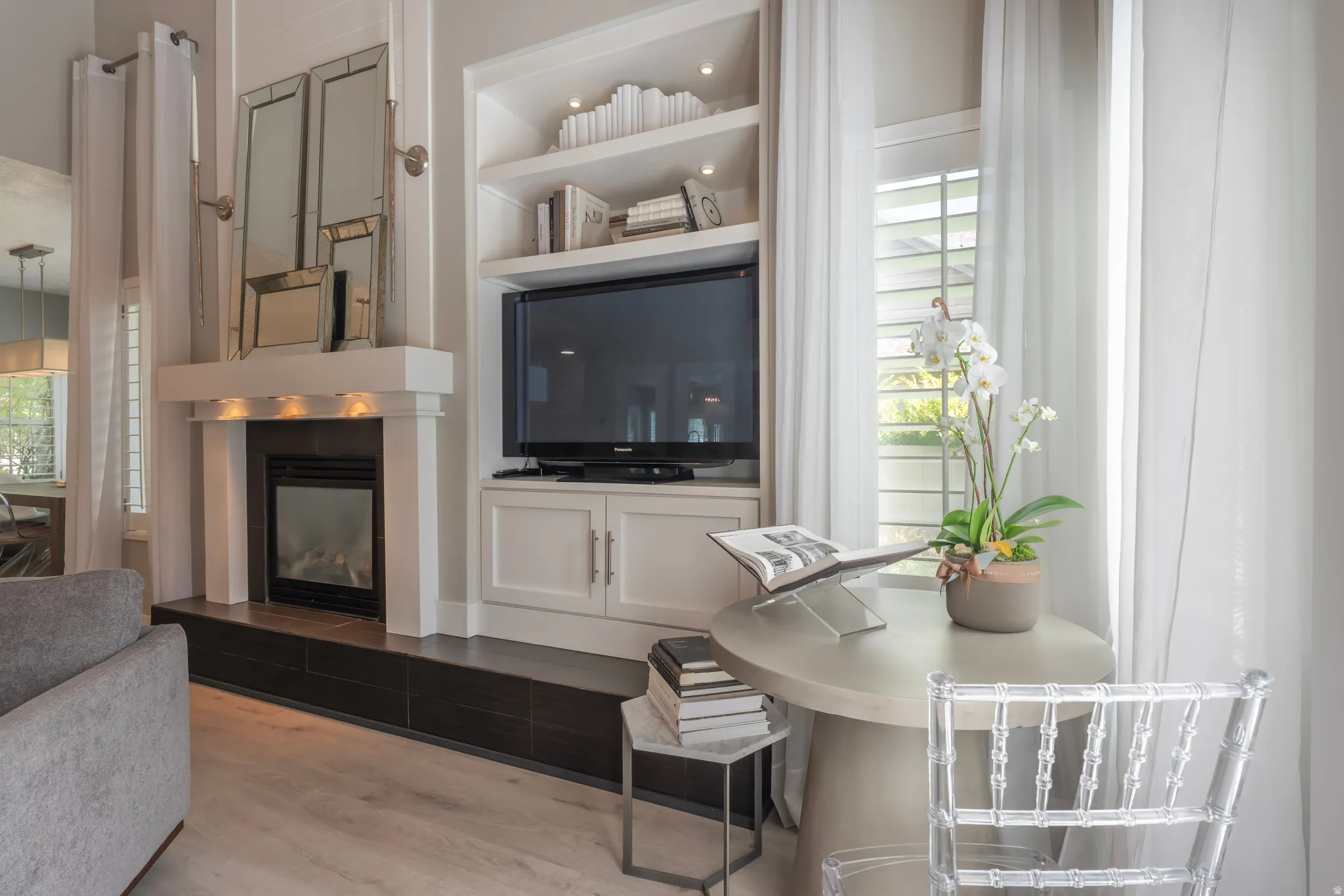 Built-in media center, integrated fireplace with dark tile surround, light wood-finish flooring, and window with plantation shutters