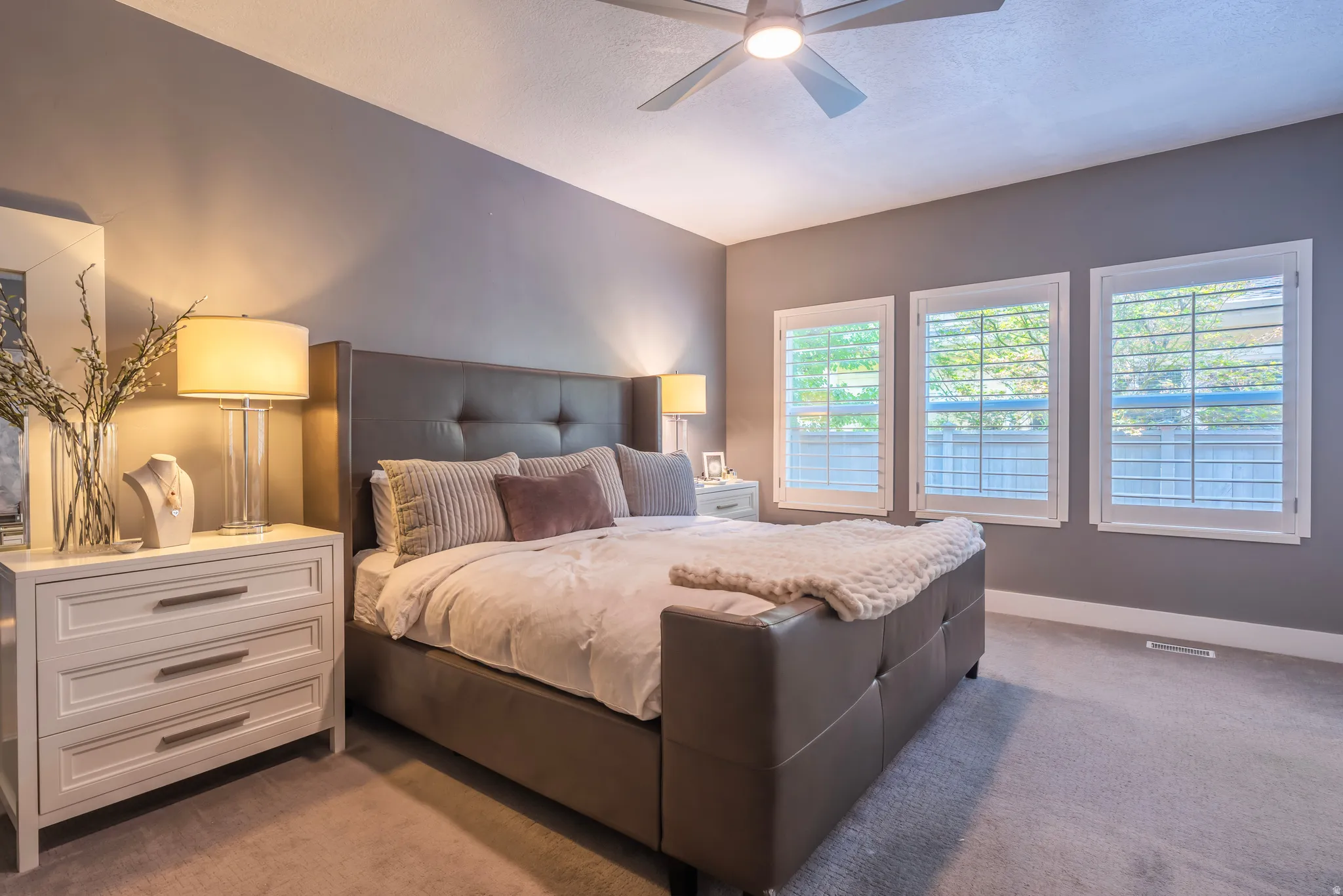 Plush carpeting, three windows with plantation shutters, ceiling fan, accent lighting, and a neutral color palette