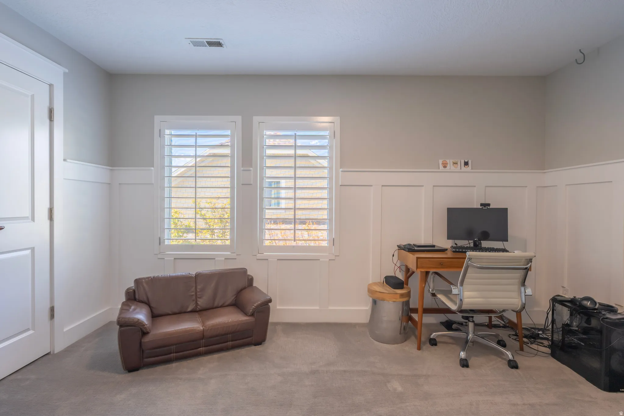 Board and batten wainscoting, two windows with plantation shutters, light-colored walls, and carpet flooring