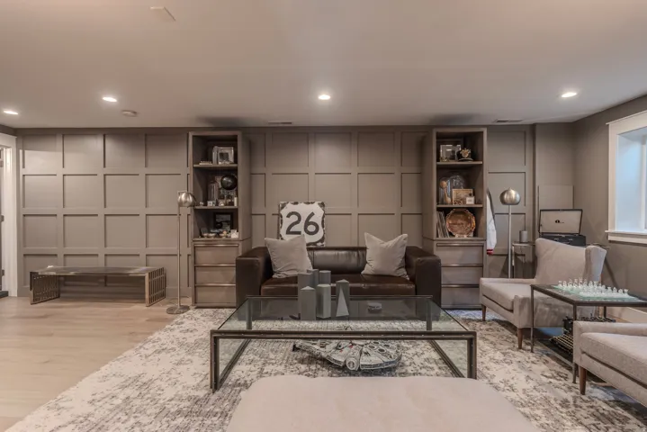Recessed lighting, wood-finish flooring, accent wall with paneling, built-in shelving, and a glass-top coffee table