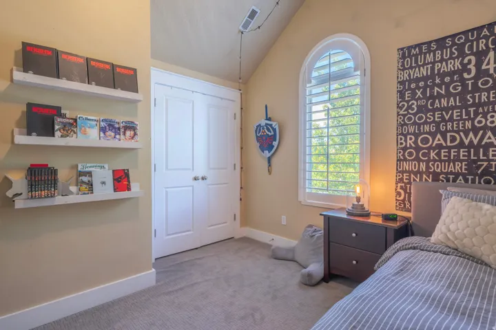Arched window with plantation shutters, built-in shelving, plush carpet, and bi-fold closet doors
