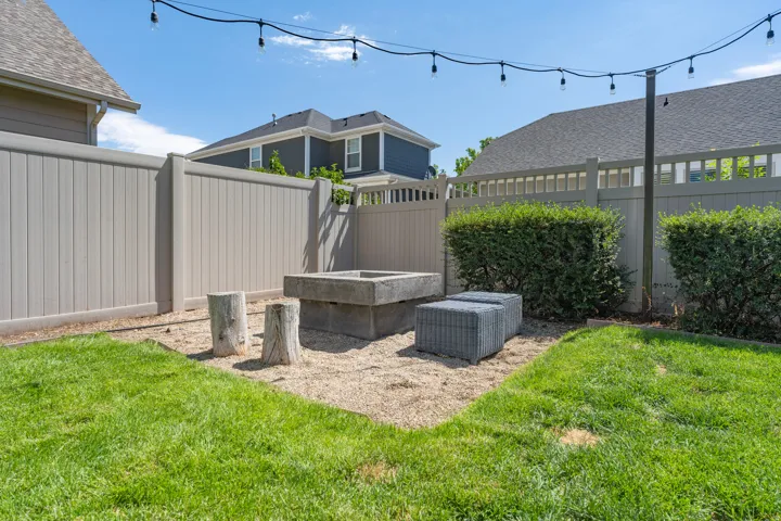 Manicured lawn with a concrete fire pit, string lighting, and privacy fencing