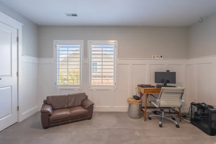 Board and batten wainscoting, two windows with plantation shutters, light-colored walls, and carpet flooring