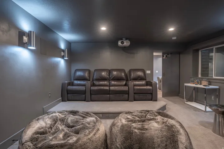 Carpeted media room with a raised platform, wall-mounted sconces, recessed lighting, and a mounted projector