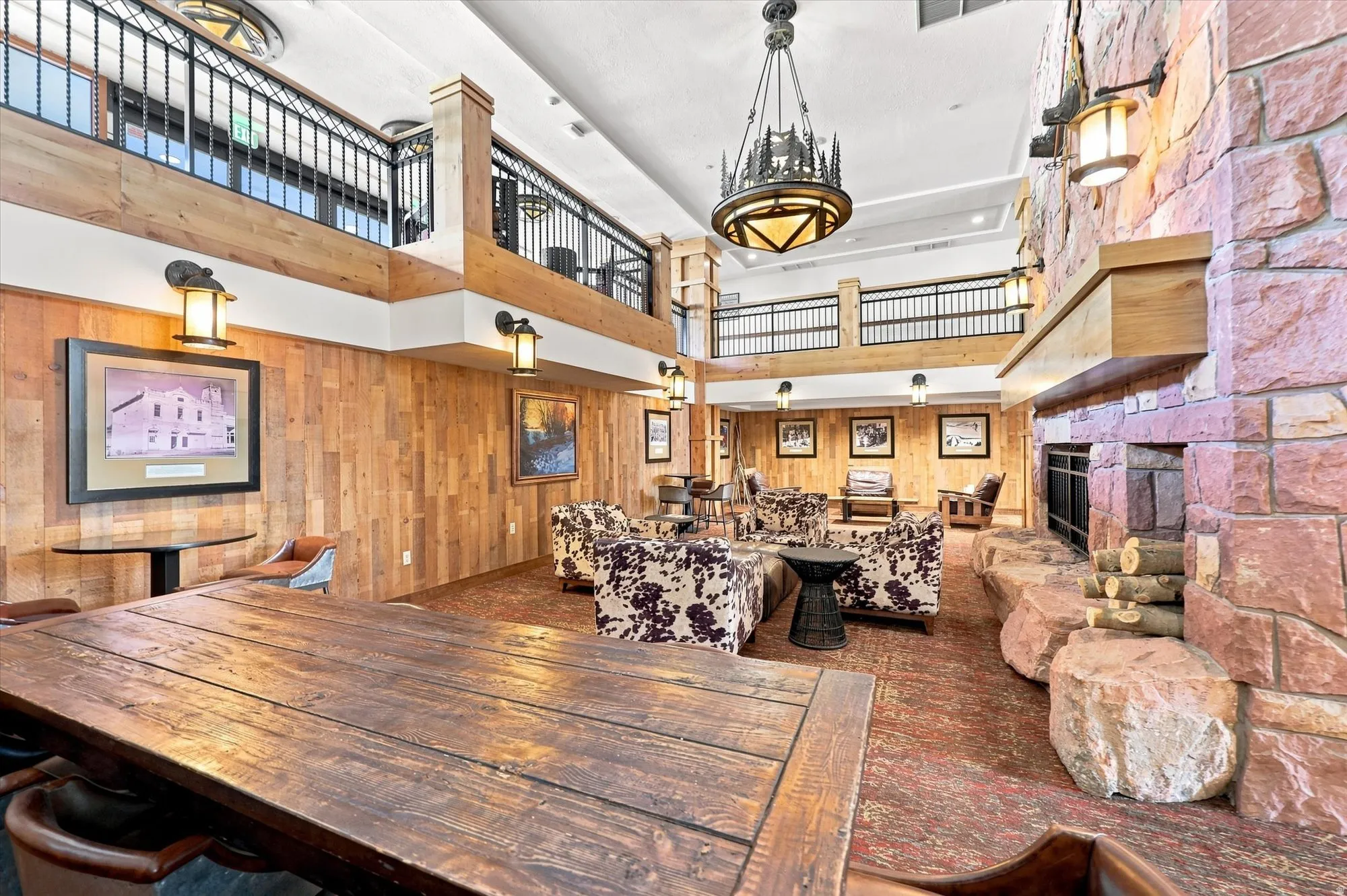 Two-story common area with stone fireplace, wood-paneled walls, exposed wood beams, and a wrought iron balcony