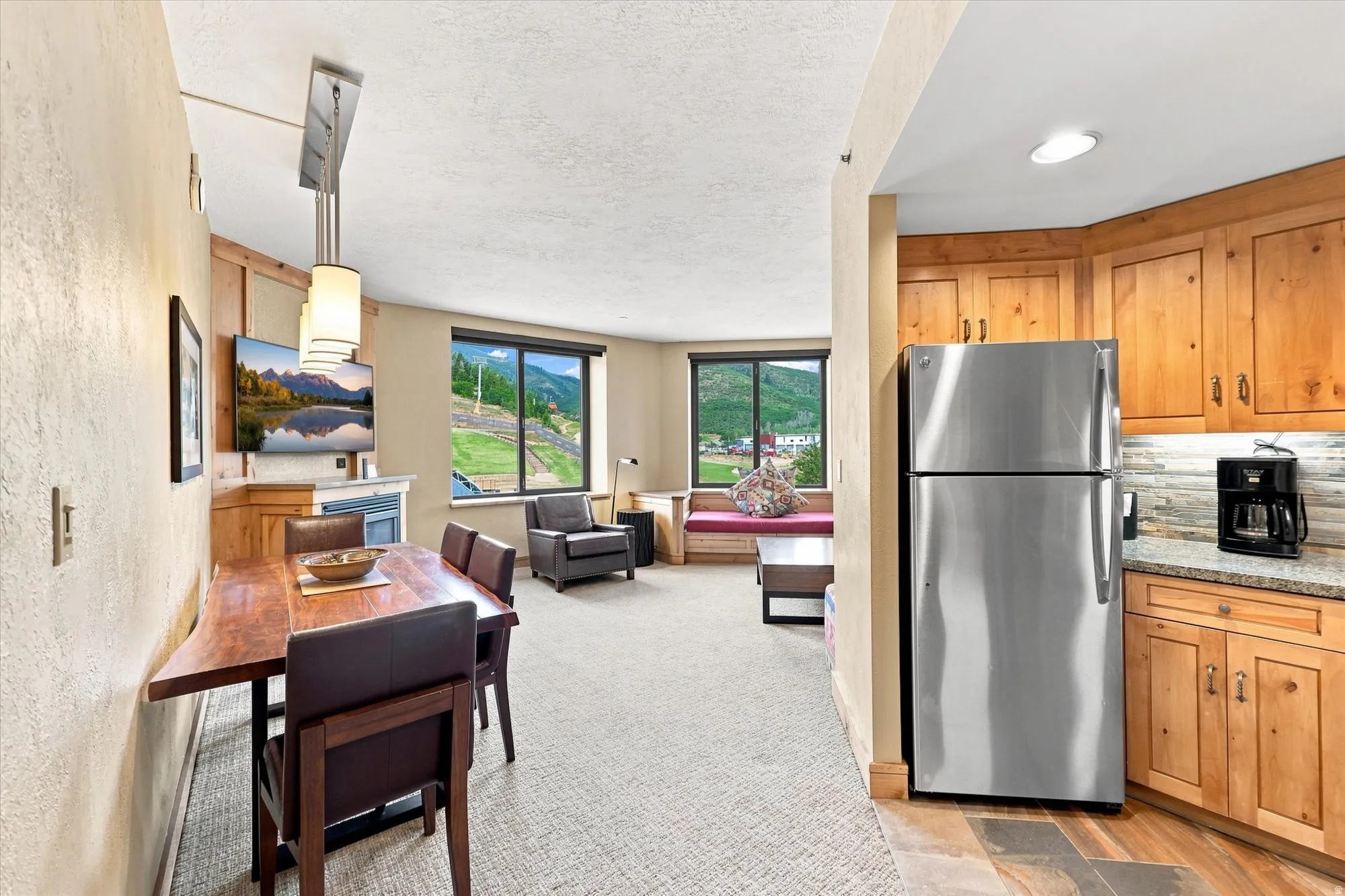 Open-concept living space with full kitchen, wood-finish cabinetry, stainless steel refrigerator, and granite-style countertops