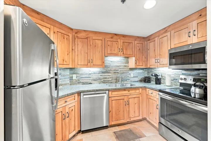 Stainless steel appliances, wood cabinetry, stone countertops, integrated sink with gooseneck faucet, and a tiled backsplash
