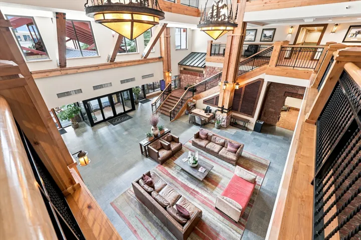 Grand multi-level lobby with exposed wood beams, slate tile flooring, dual staircases with wrought iron railings, and large decorative chandeliers