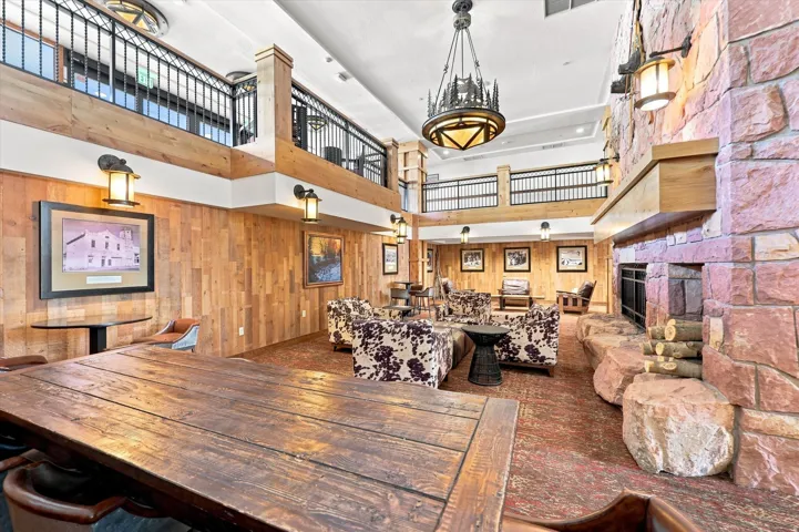Two-story common area with stone fireplace, wood-paneled walls, exposed wood beams, and a wrought iron balcony
