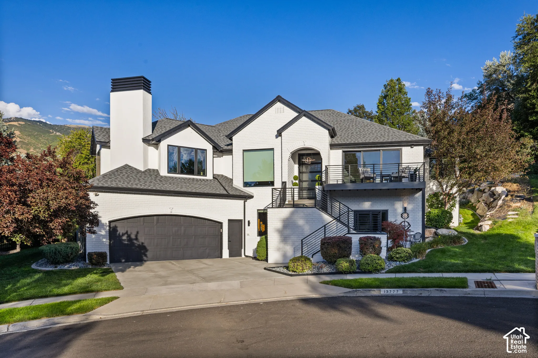 Modern dwelling with white brick exterior, black trim, arched garage, multiple balconies, and professional landscaping
