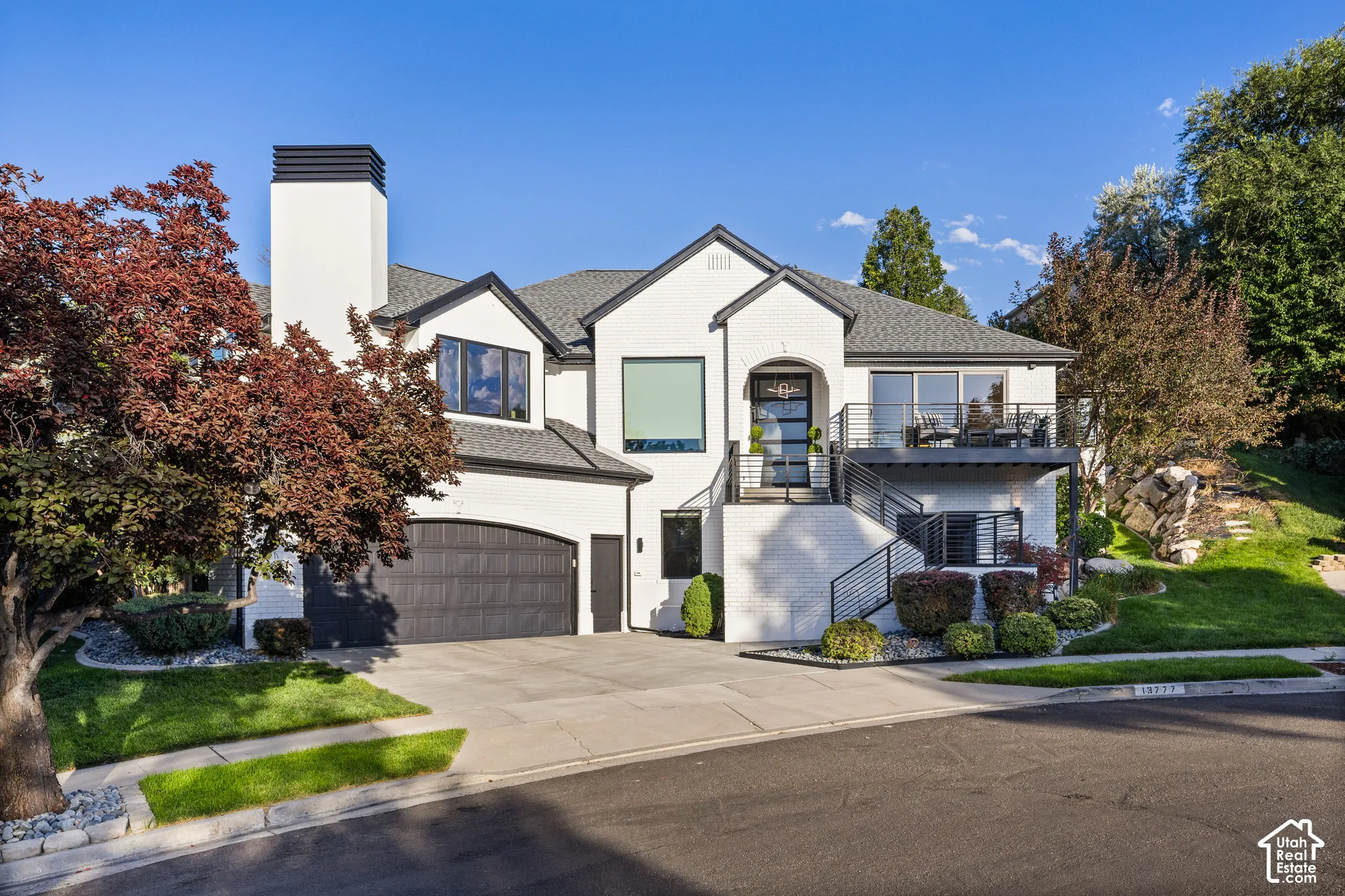 Modern exterior with white brick, dark trim, an arched garage door, and a second-story balcony with metal railings