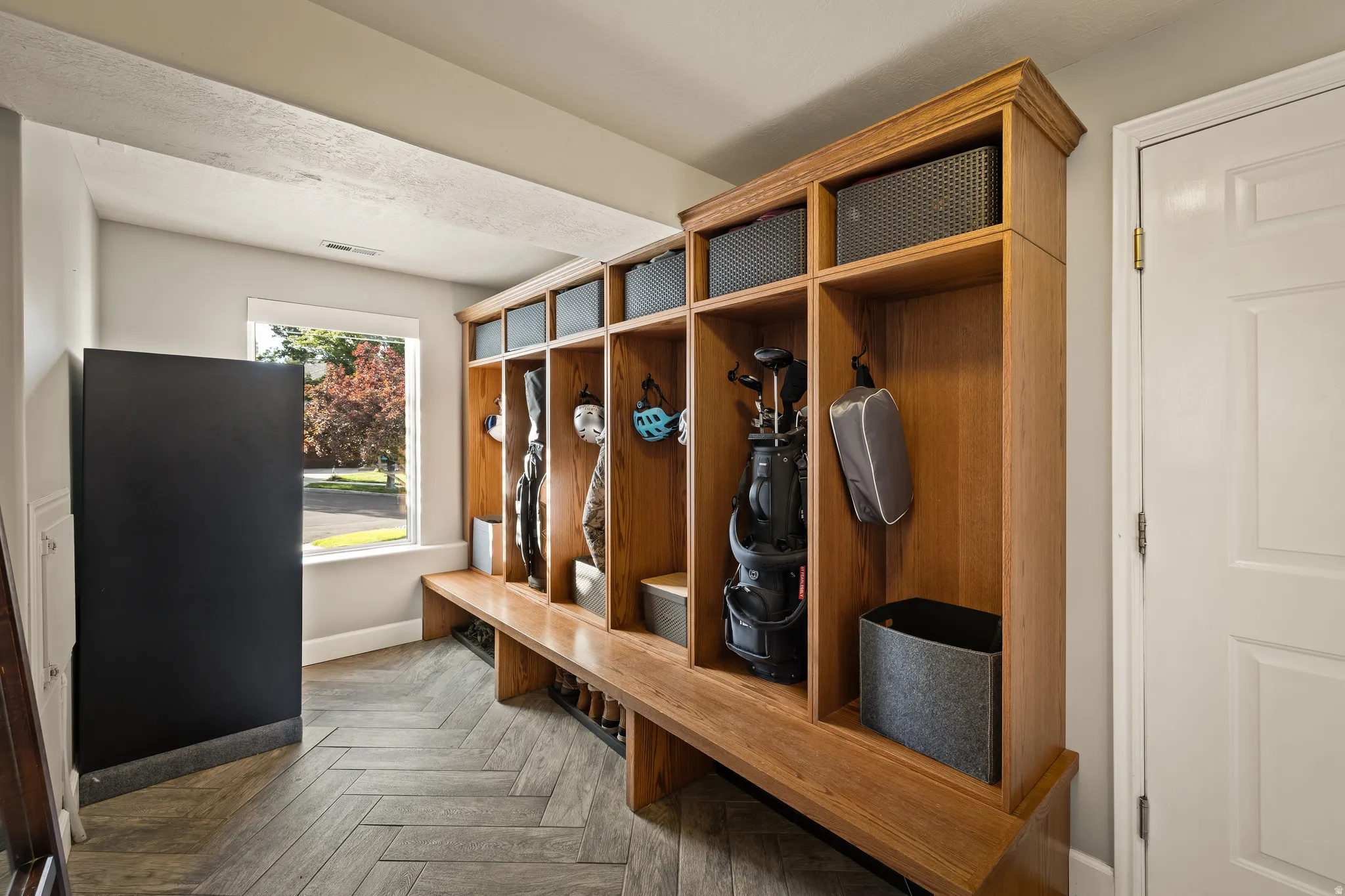 Wood-finish flooring in a herringbone pattern, custom built-in wood lockers with integrated bench seating, and a window providing natural light