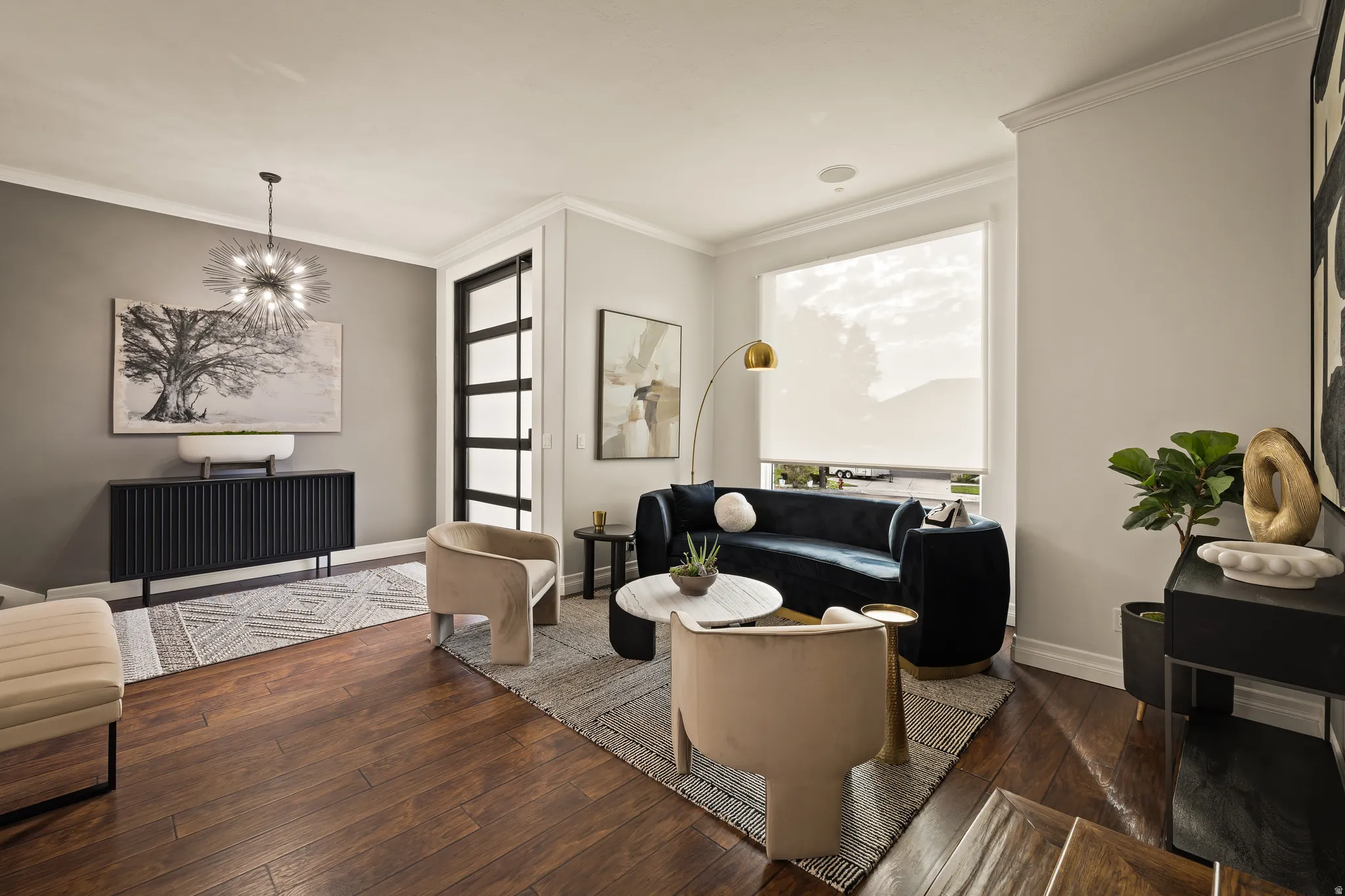 Hardwood flooring, crown molding, modern chandelier, large window with roller shade, and built-in wall speaker