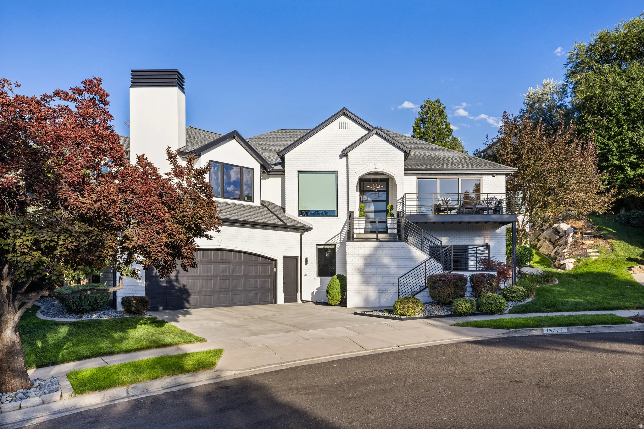 Modern exterior with white brick, dark trim, an arched garage door, and a second-story balcony with metal railings