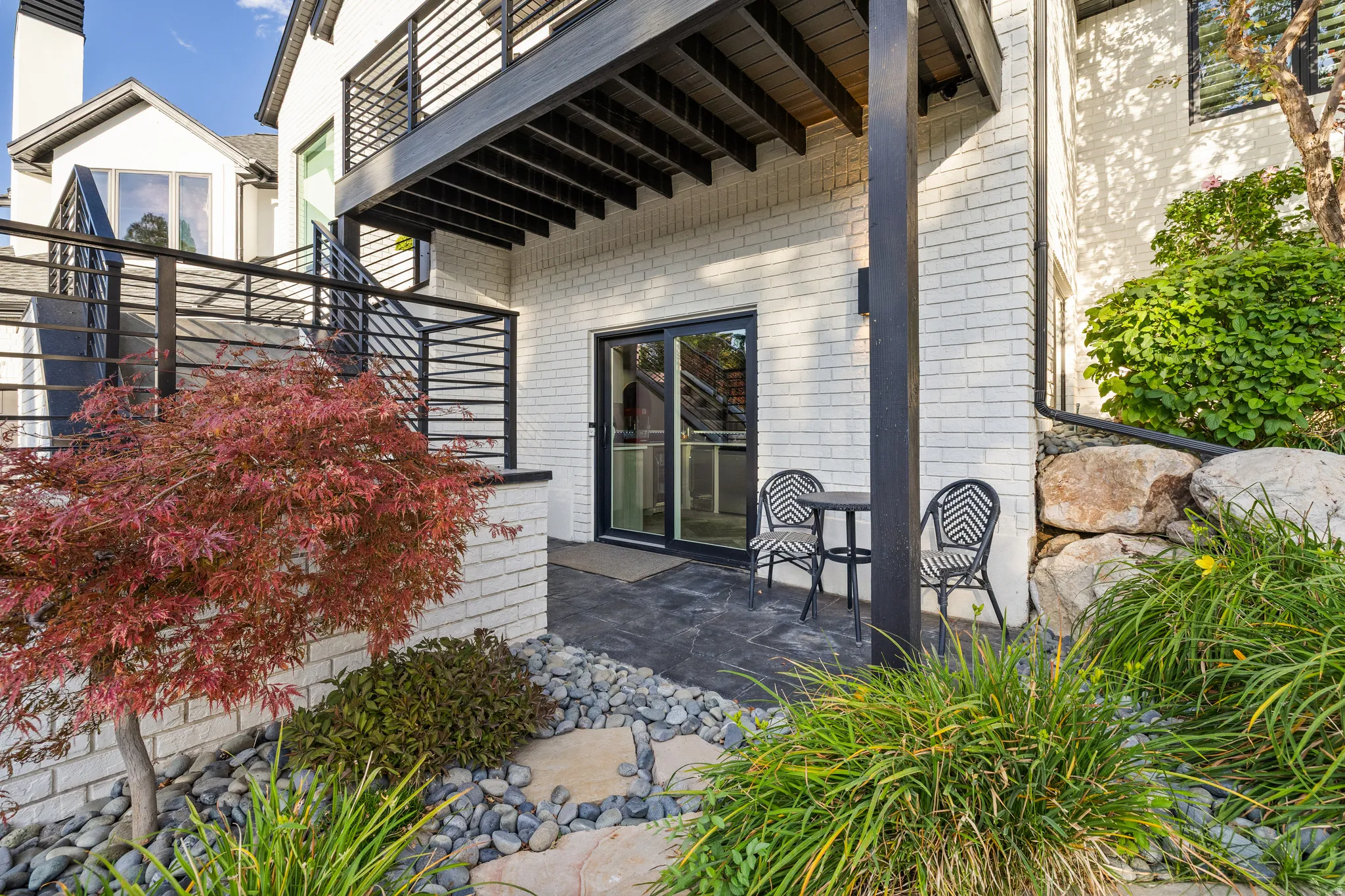 Lower level patio with a sliding glass door, white brick exterior, black horizontal railing, and surrounding landscaping