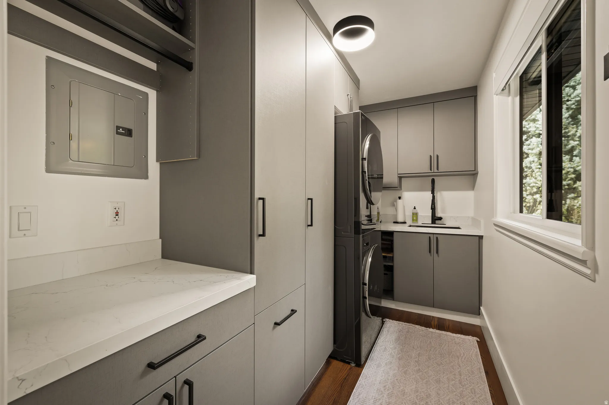 Built-in gray cabinetry, integrated stacked washer and dryer, white countertops, single basin sink with a black gooseneck faucet, and wood-finish flooring