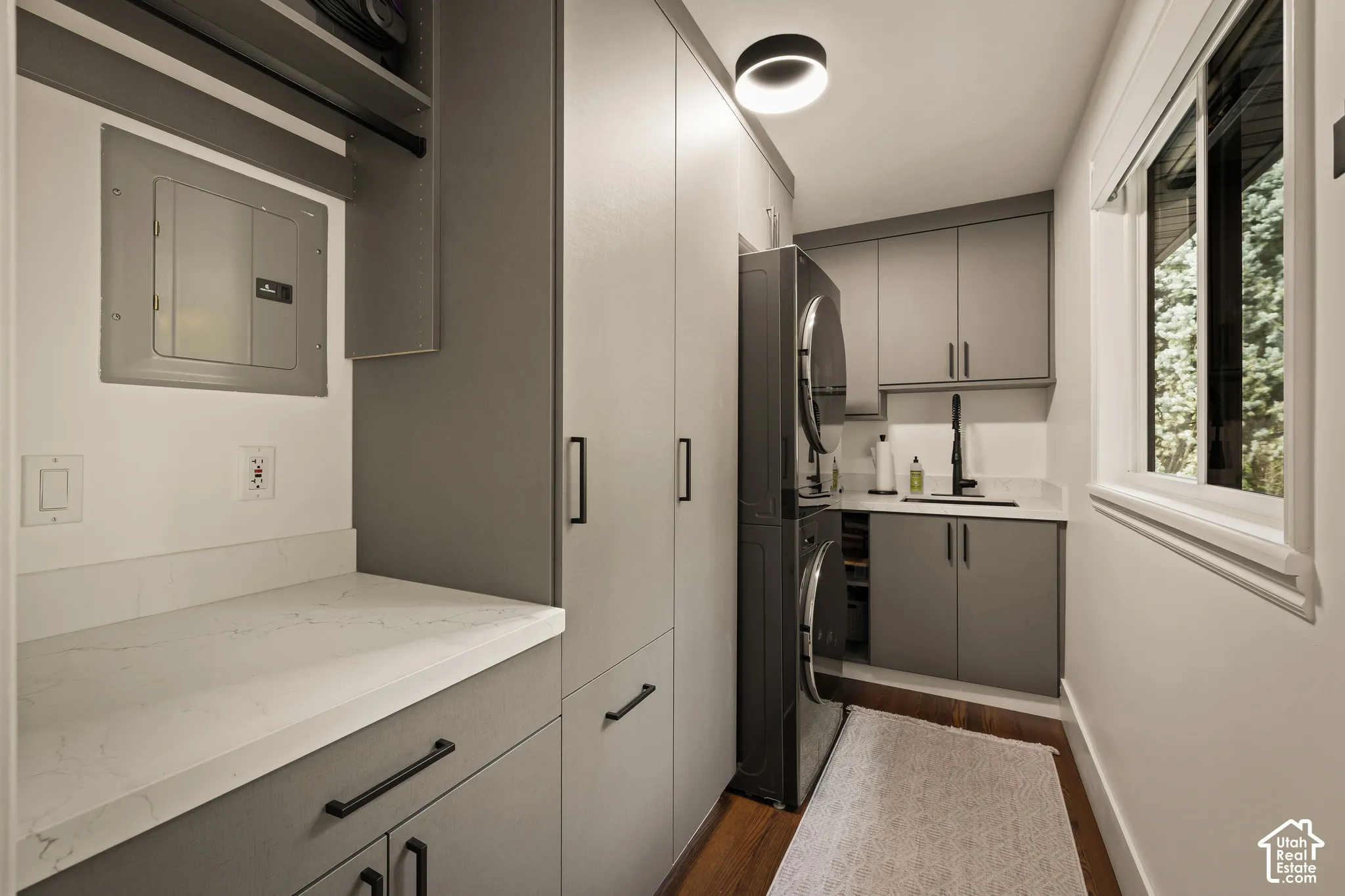 Built-in gray cabinetry, integrated stacked washer and dryer, white countertops, single basin sink with a black gooseneck faucet, and wood-finish flooring