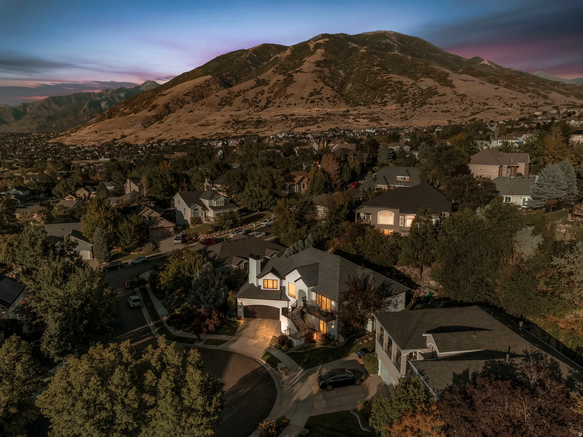 Expansive mountain backdrop, residential neighborhood setting, mature trees, multi-level dwelling, attached garage