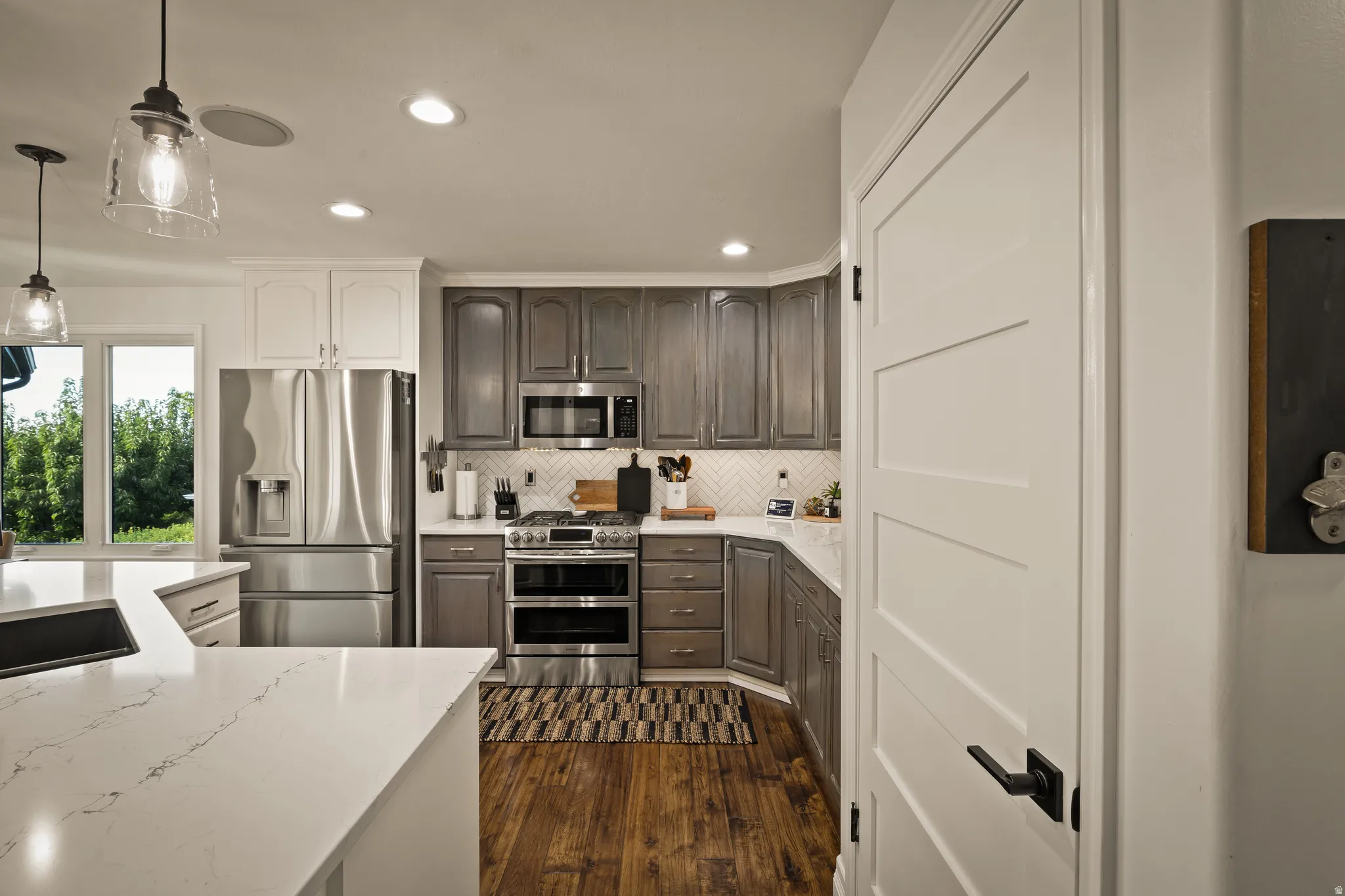 Kitchen featuring stainless steel appliances, wood-finish flooring, quartz countertops, pendant lighting, and recessed lighting