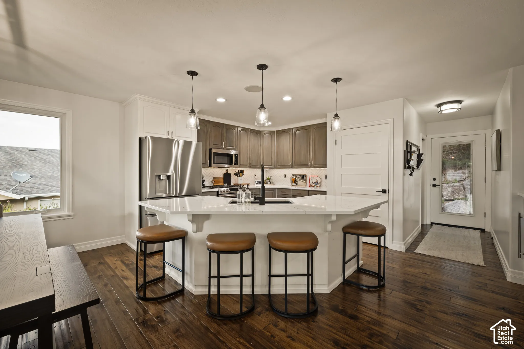 Kitchen featuring a multi-sided island with pendant lighting, stainless steel appliances, wood-finish flooring, and white cabinetry