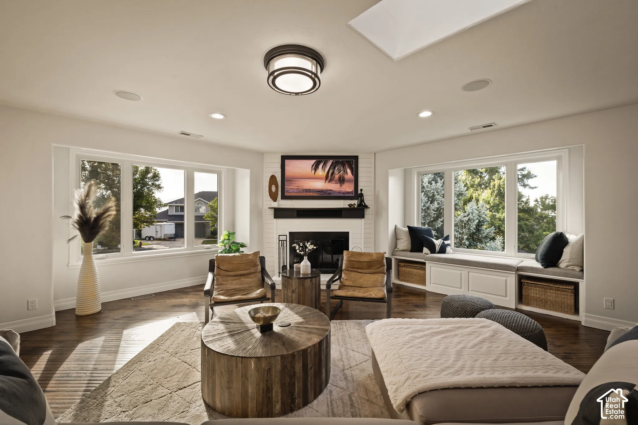 White brick fireplace with a dark mantel, wood-finish flooring, recessed lighting, and a skylight