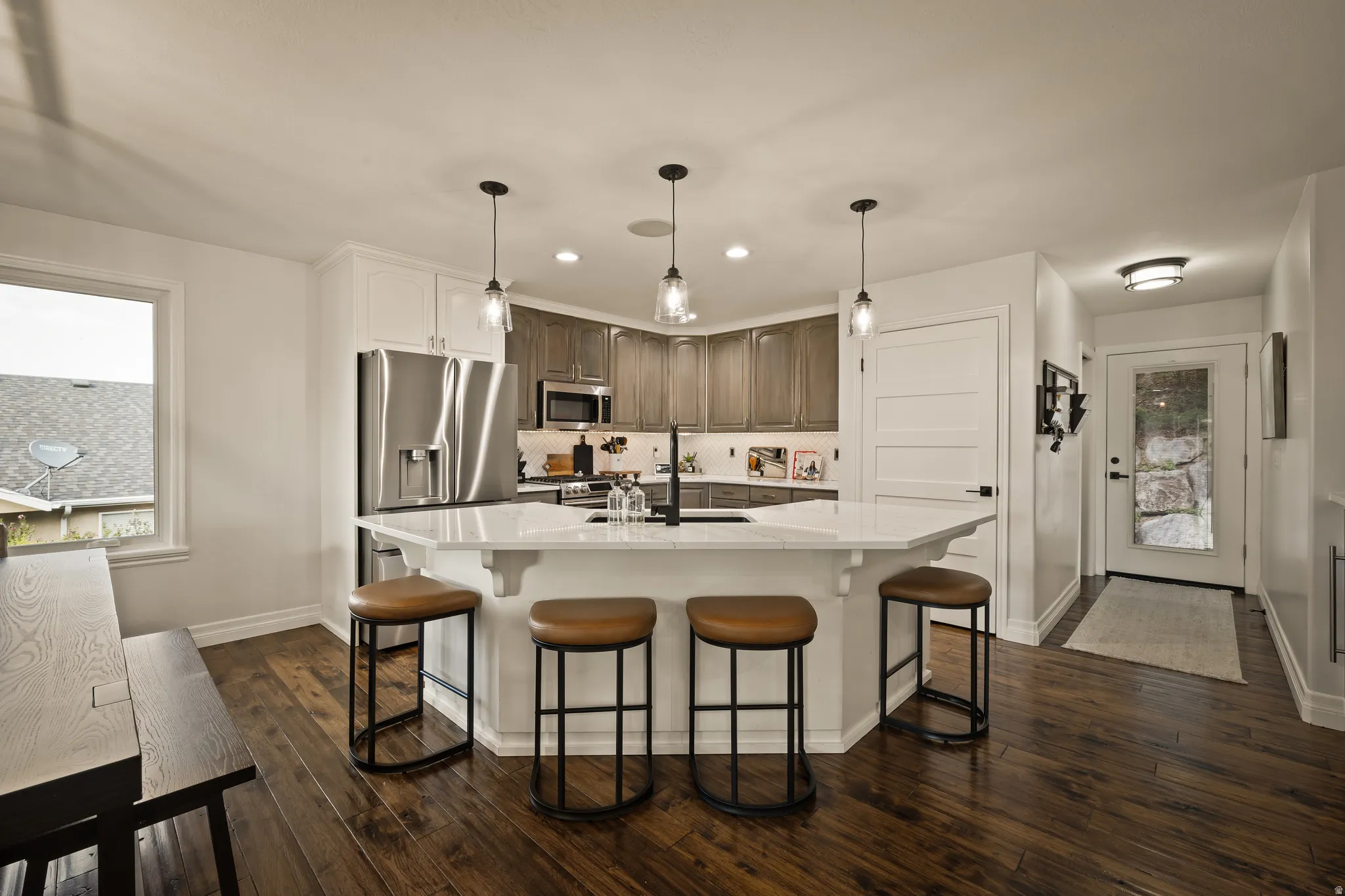 Kitchen featuring a multi-sided island with pendant lighting, stainless steel appliances, wood-finish flooring, and white cabinetry