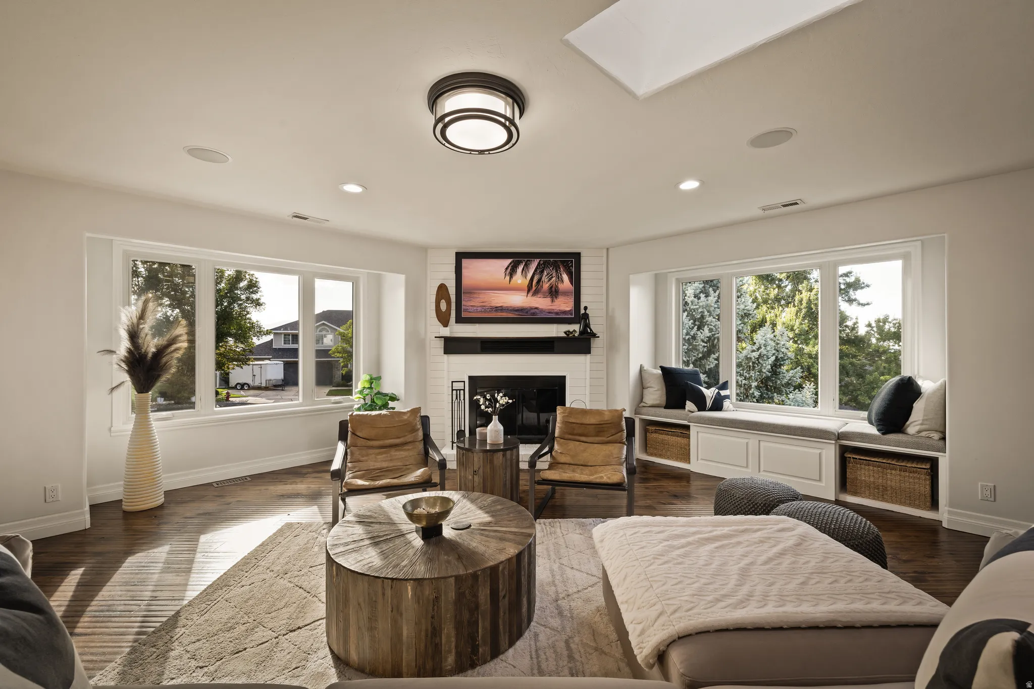 White brick fireplace with a dark mantel, wood-finish flooring, recessed lighting, and a skylight