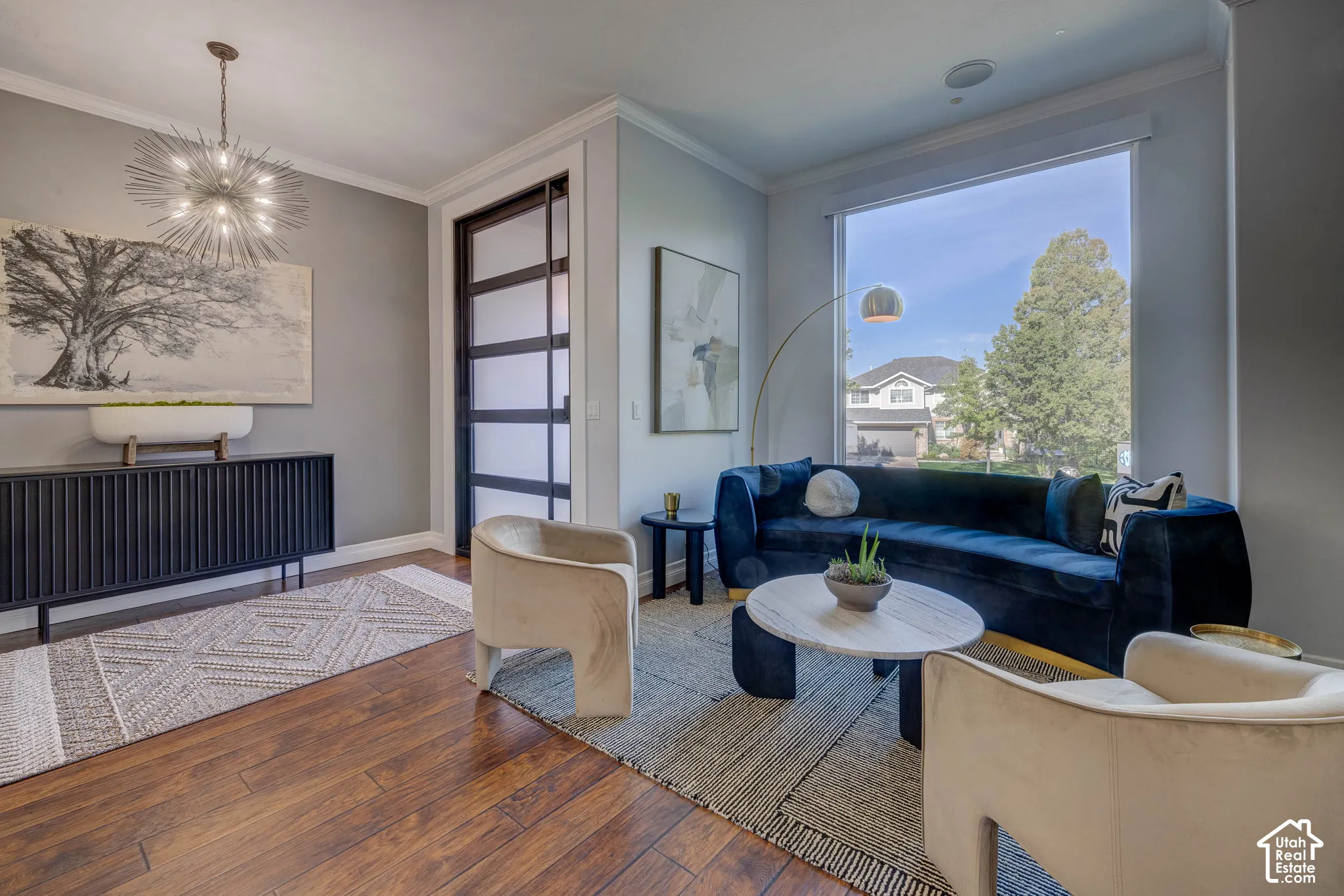 Wood-finish flooring, accent wall with framed artwork, modern chandelier, large window with ample natural light, and a built-in speaker