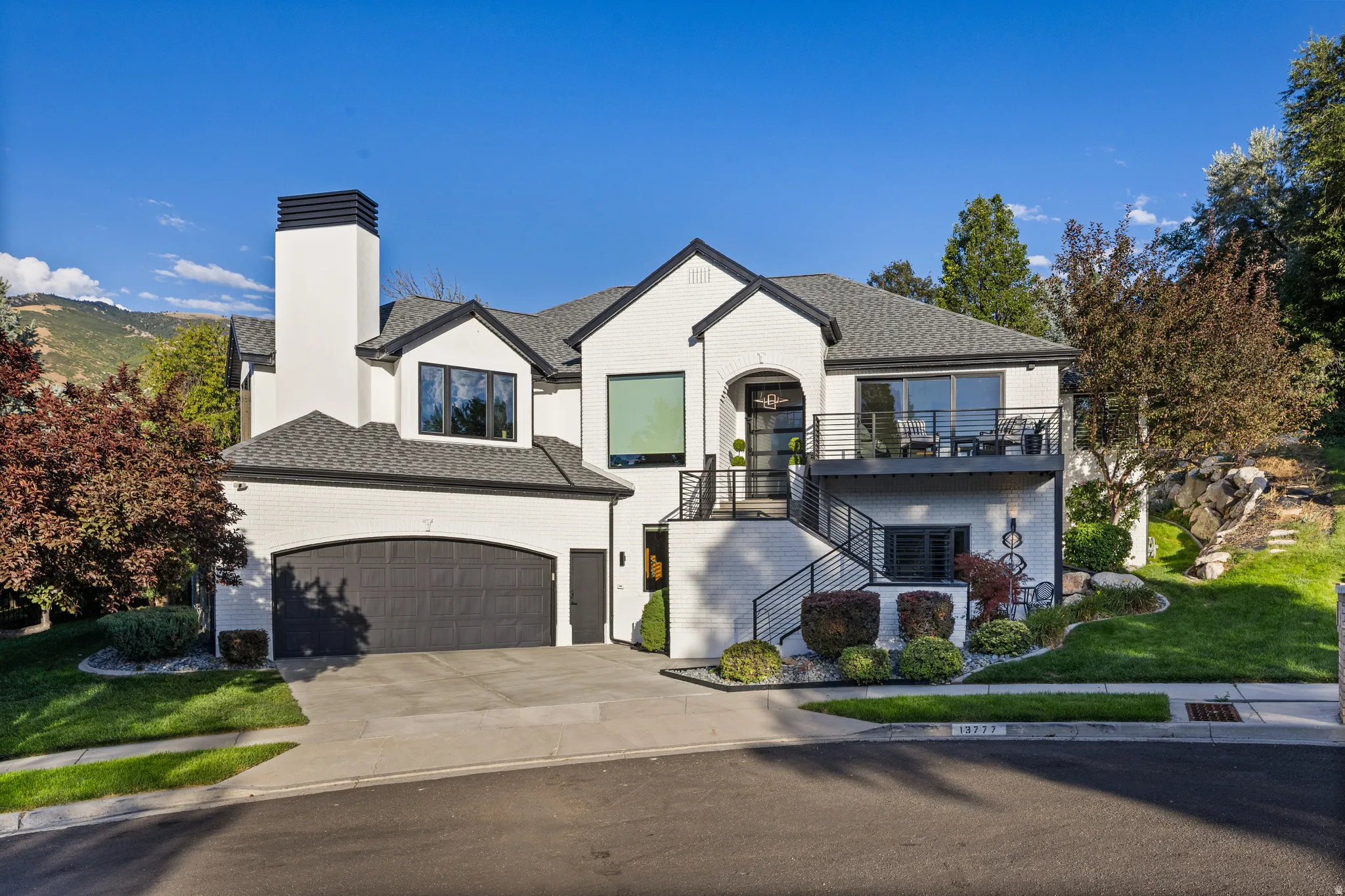 Modern dwelling with white brick exterior, black trim, arched garage, multiple balconies, and professional landscaping