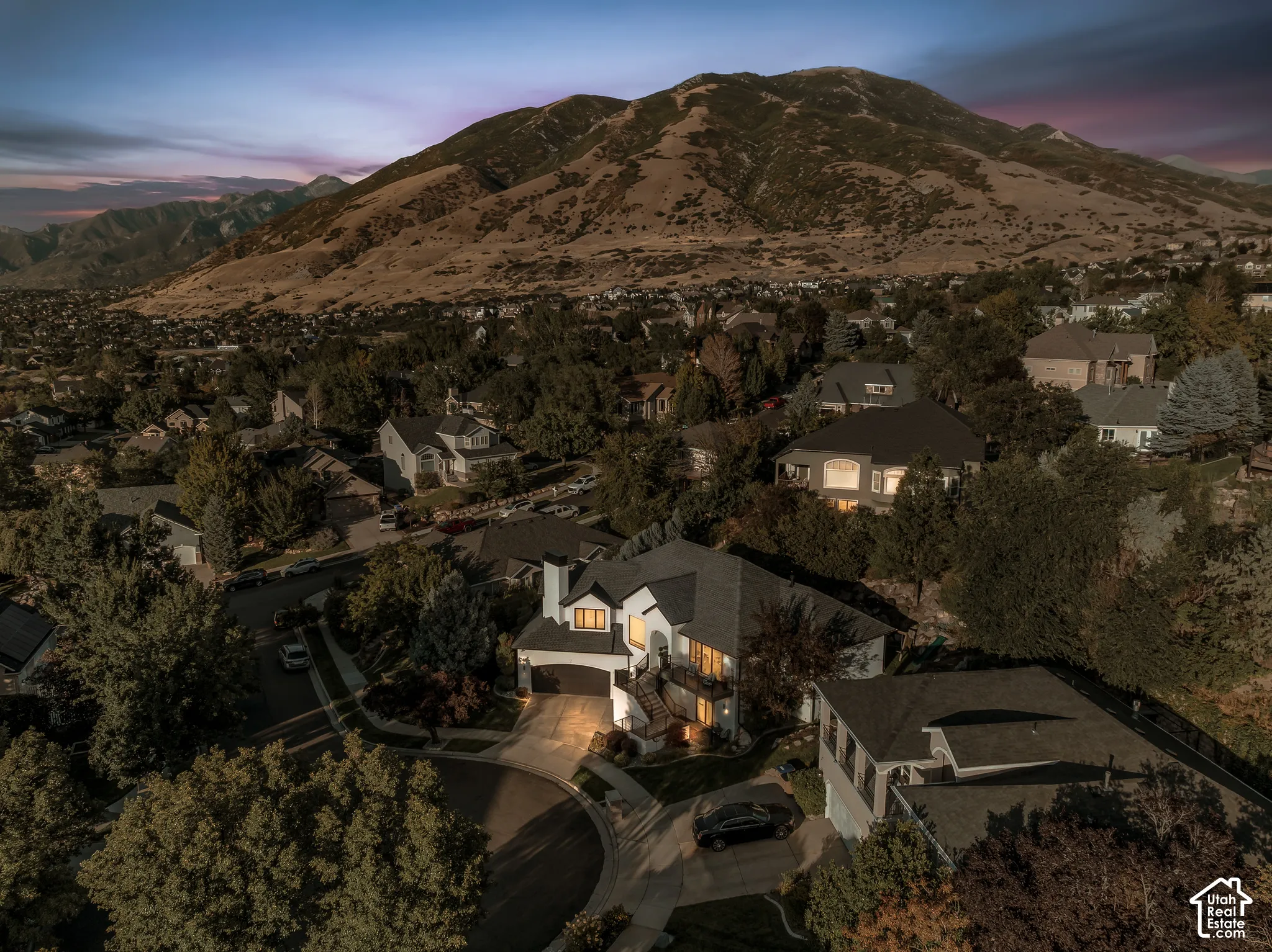 Expansive mountain backdrop, residential neighborhood setting, mature trees, multi-level dwelling, attached garage
