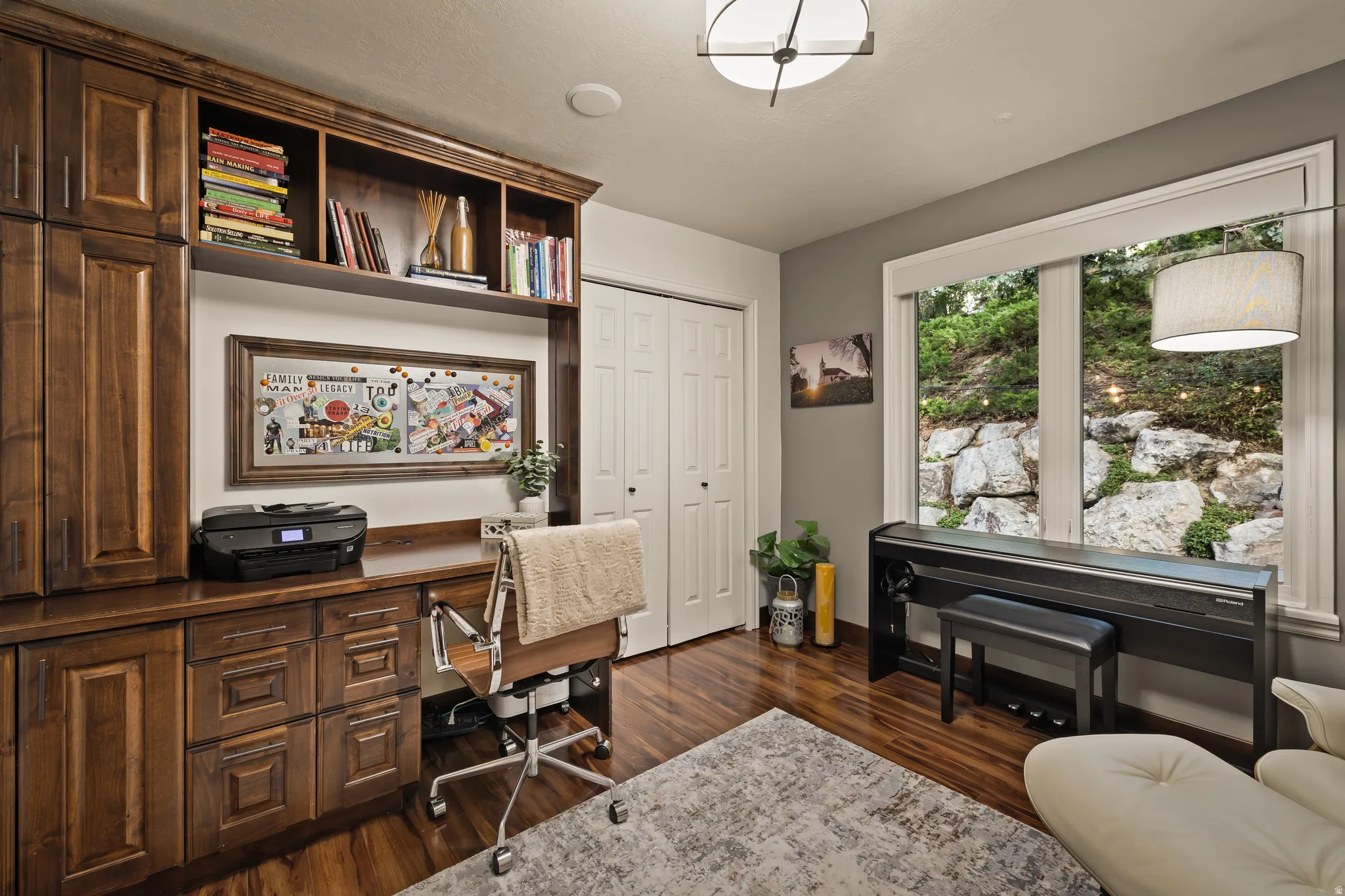 Built-in cabinetry and shelving, hardwood-finish flooring, white bi-fold closet doors, and large windows with natural rock landscaping