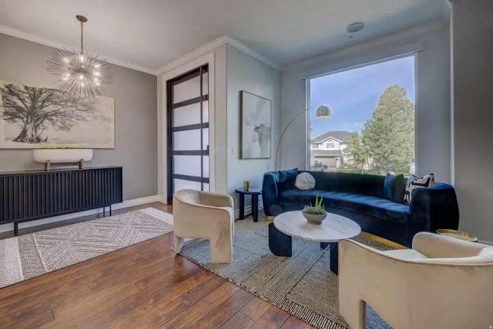 Wood-finish flooring, accent wall with framed artwork, modern chandelier, large window with ample natural light, and a built-in speaker
