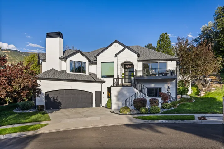 Modern dwelling with white brick exterior, black trim, arched garage, multiple balconies, and professional landscaping