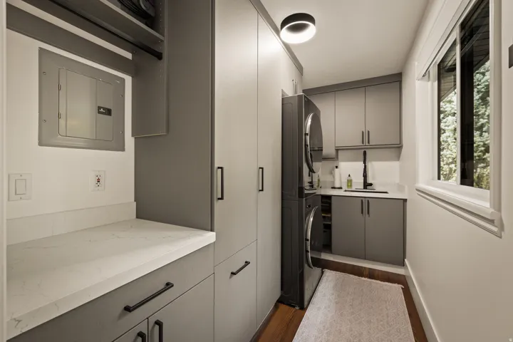Built-in gray cabinetry, integrated stacked washer and dryer, white countertops, single basin sink with a black gooseneck faucet, and wood-finish flooring