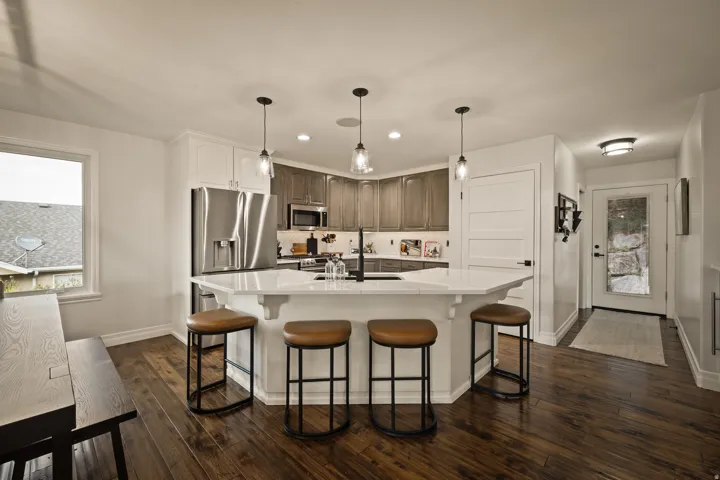 Kitchen featuring a multi-sided island with pendant lighting, stainless steel appliances, wood-finish flooring, and white cabinetry