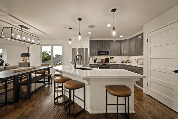 Gourmet kitchen with a large island, stainless steel appliances, wood-finish flooring, and pendant lighting