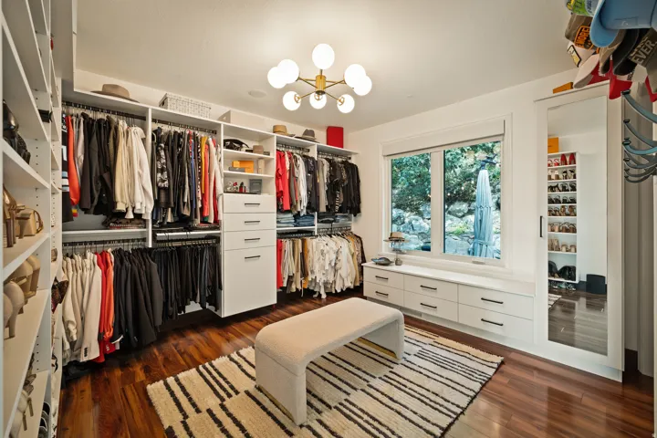 Custom built-in closet systems with integrated drawers, wood-finish flooring, a contemporary ceiling light fixture, a large window, and a full-length mirrored sliding door