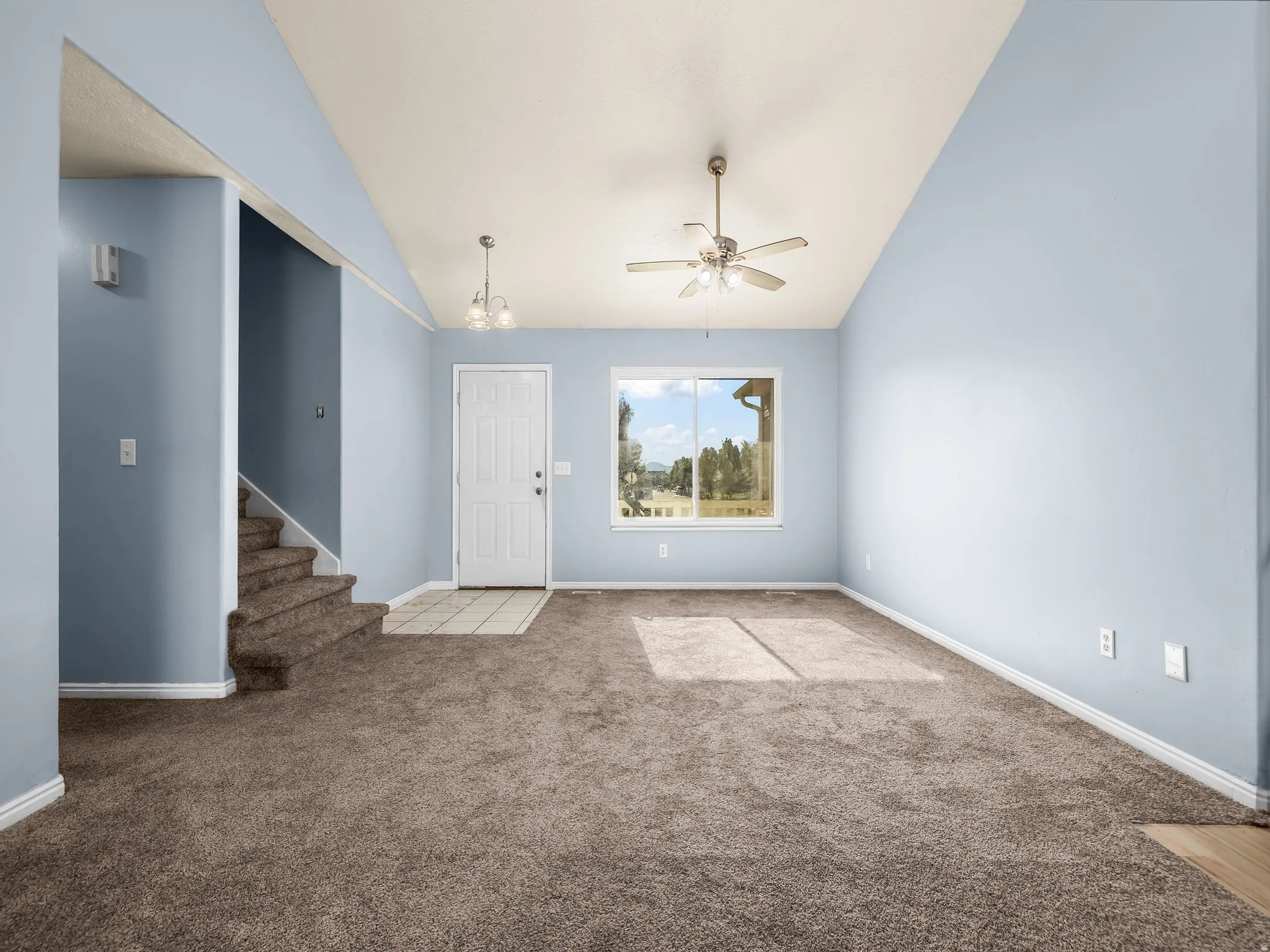 Vaulted ceiling, ceiling fan, white door, window with outdoor scenery, tiled entry