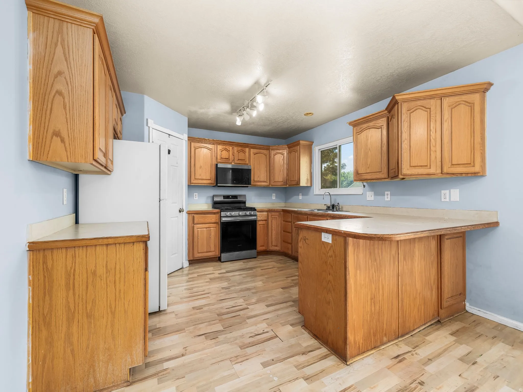 Well-appointed kitchen featuring light wood cabinetry, a U-shaped countertop configuration, a built-in oven, and wood-finish flooring
