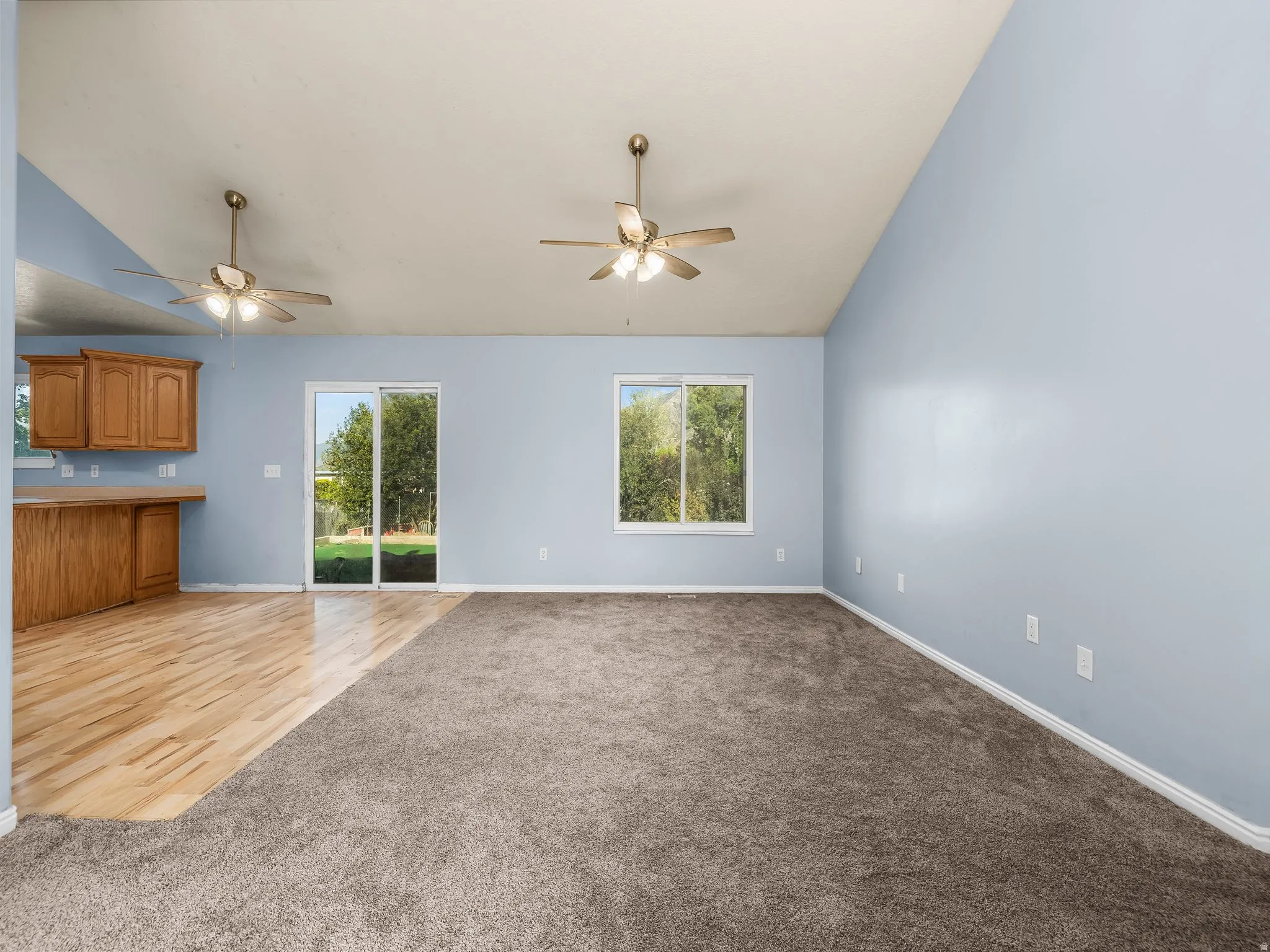 Vaulted ceilings with two ceiling fans, mixed flooring with wood-finish and carpet, sliding glass door, and a window providing exterior views