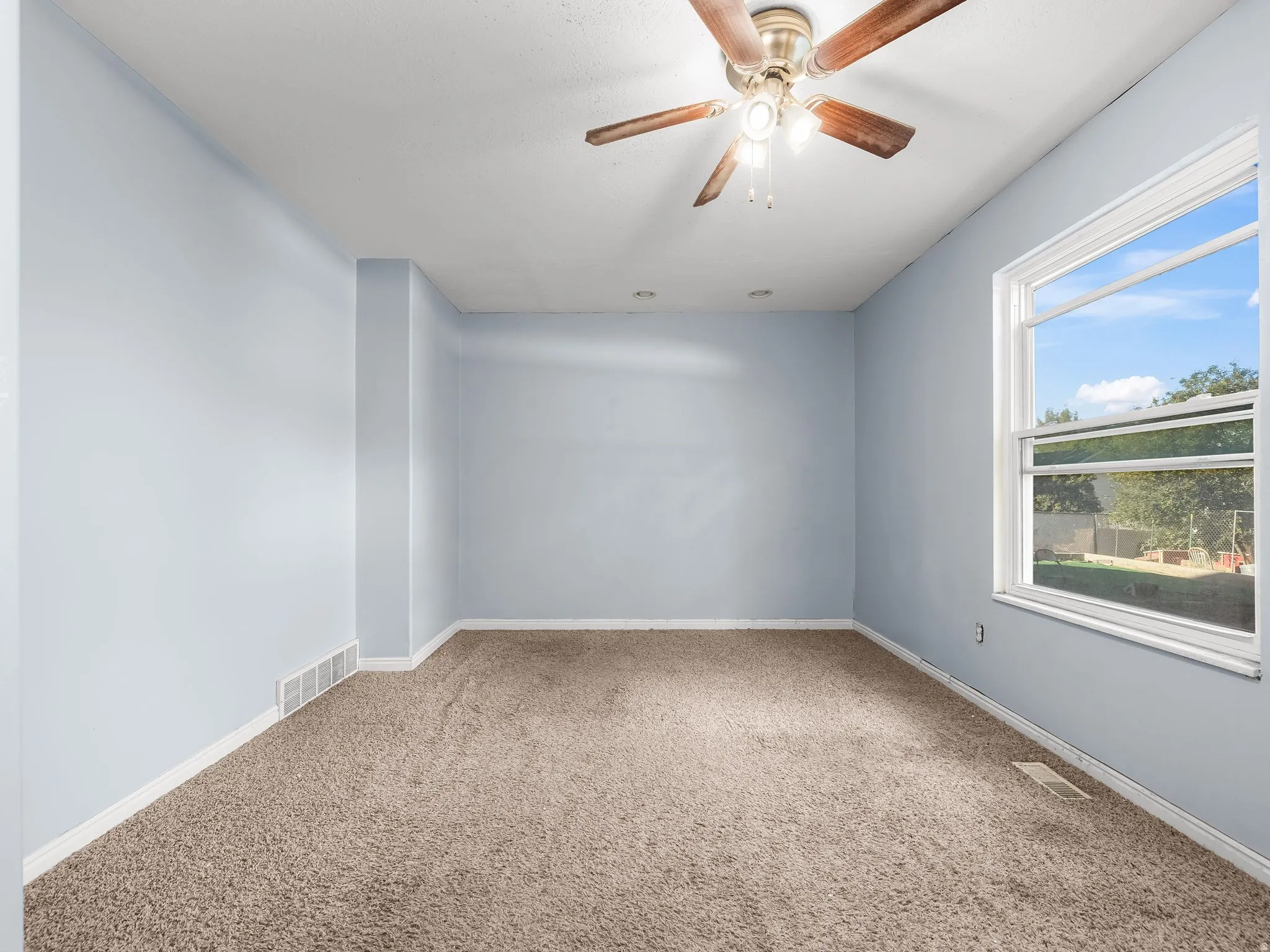 Ceiling fan with wood-finish blades, large window, and carpeted flooring